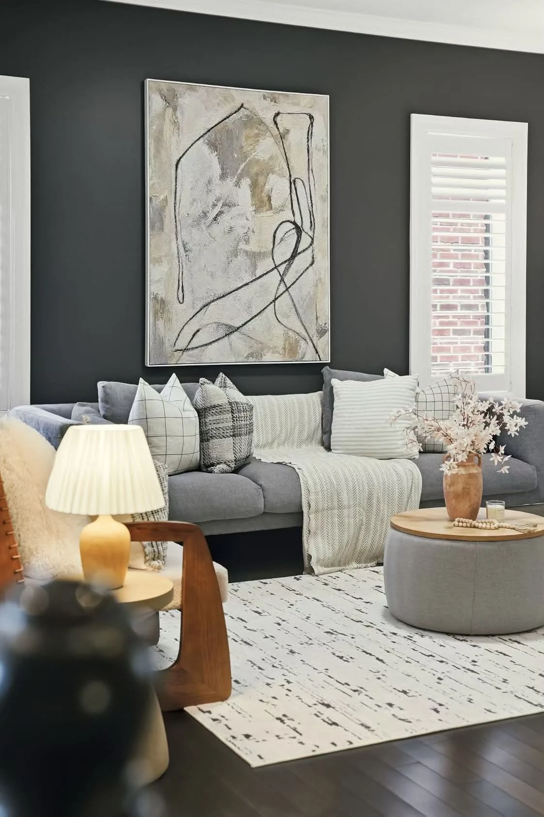Living room with a charcoal accent wall, abstract artwork and a grey sofa with layered cushions