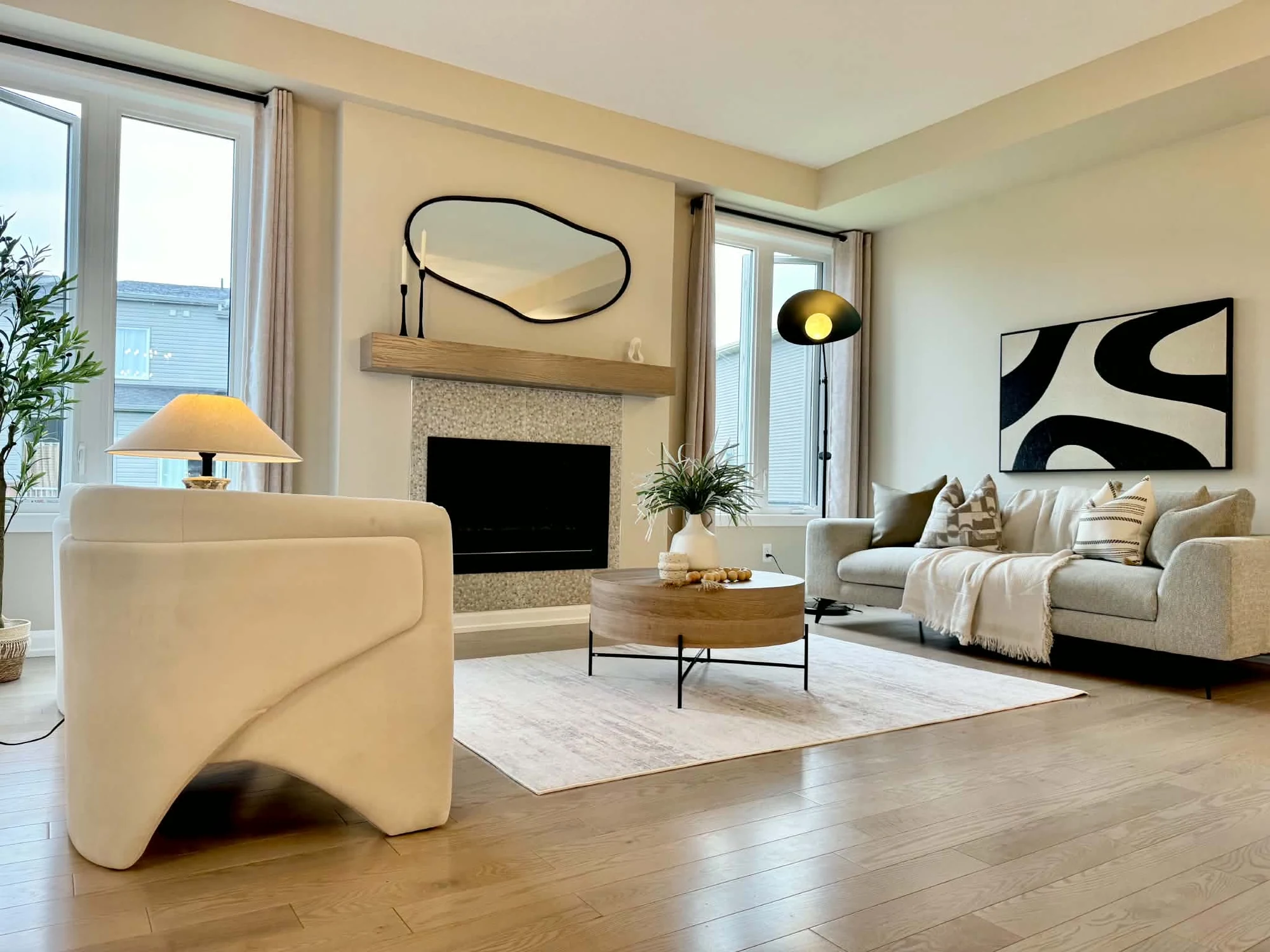 Neutral living room with a curved cream chair, grey sofa, wood coffee table and fireplace